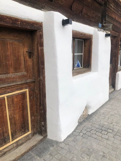 Eine weiße Wand mit Holztüren und -fenstern auf einem gepflasterten Gehweg.