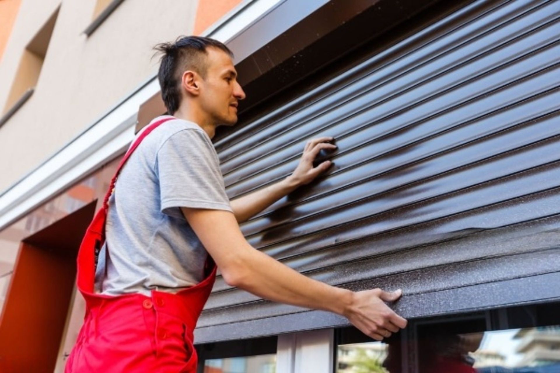 Un hombre con un mono rojo está instalando una persiana en una ventana.