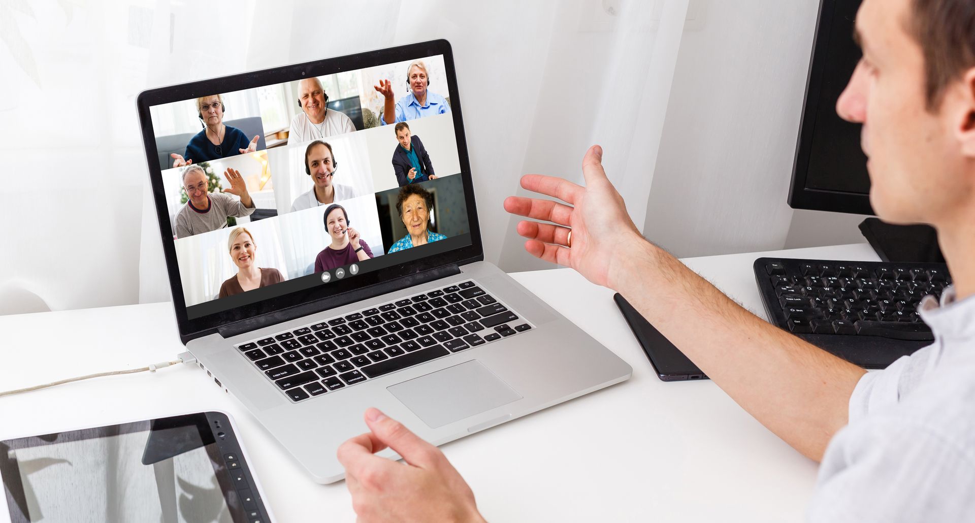 Ein Mann sitzt an einem Schreibtisch und nutzt einen Laptop, um mit einer Gruppe von Leuten per Videoanruf zu sprechen.