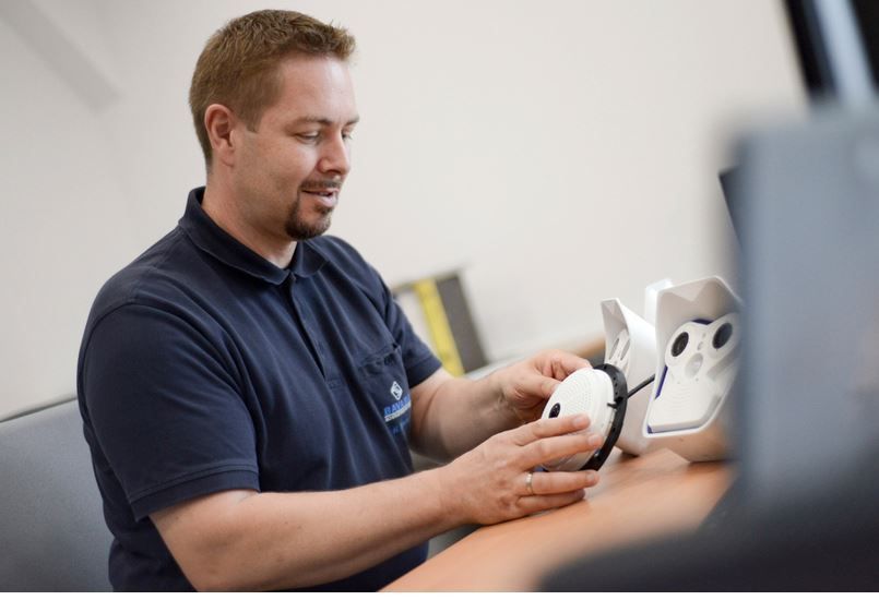 Mann im blauen Hemd montiert ein weißes VR-Headset und sitzt an einem Schreibtisch.