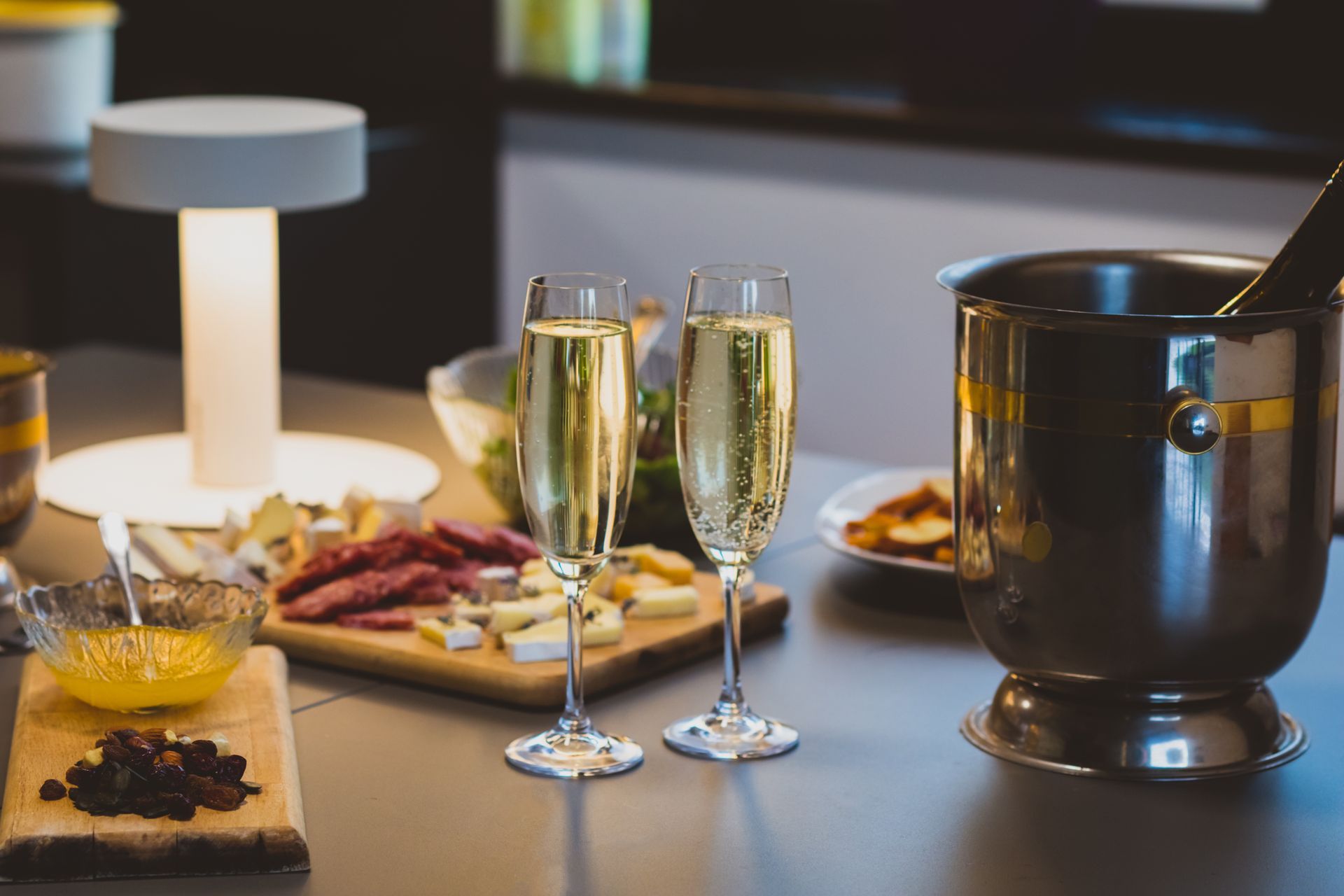 Élégante table dressée avec flûtes à champagne, lampe, amuse-gueules et seau à vin dans un restaurant à l'ambiance tamisée.
