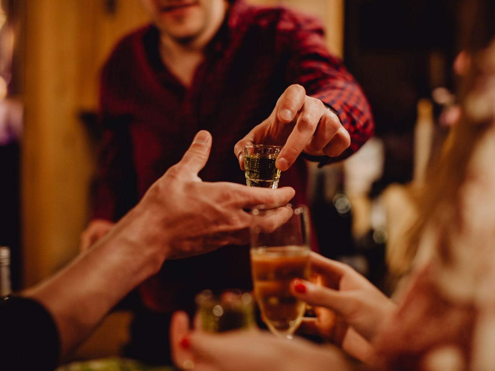 Des mains qui se passent et des petits verres qui s'entrechoquent autour d'une table de fête chaleureuse et faiblement éclairée