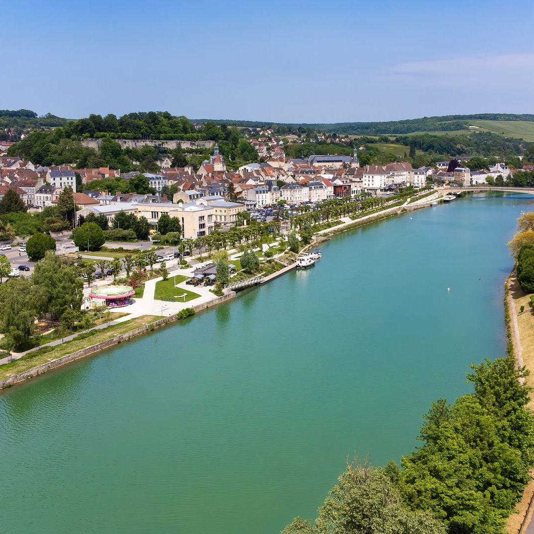 Ville riveraine aux bâtiments aux toits rouges bordant une large rivière verdoyante et des berges arborées