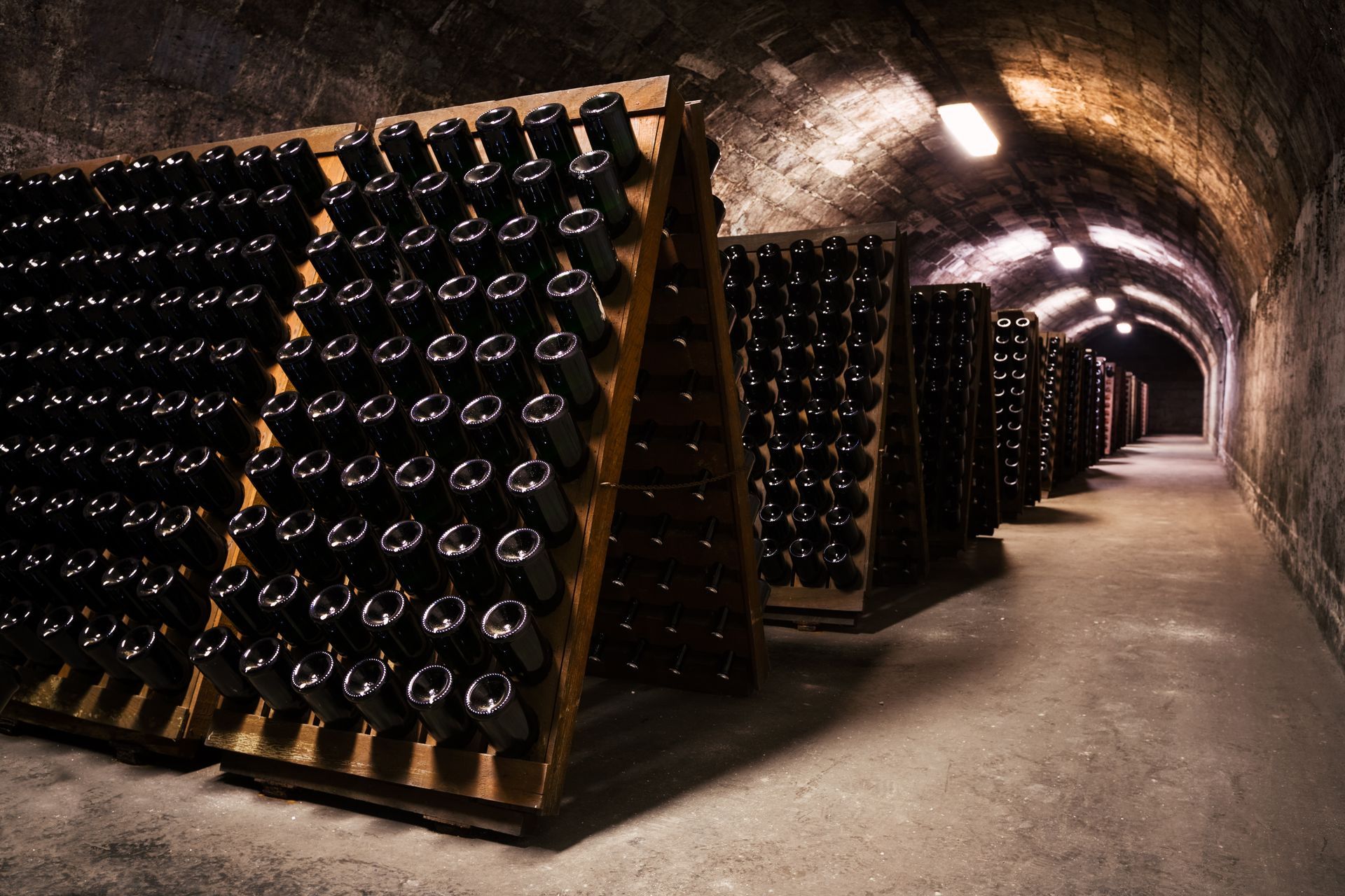 Des rangées de bouteilles de vin sont entreposées sur des étagères dans un tunnel de cave souterrain sombre.