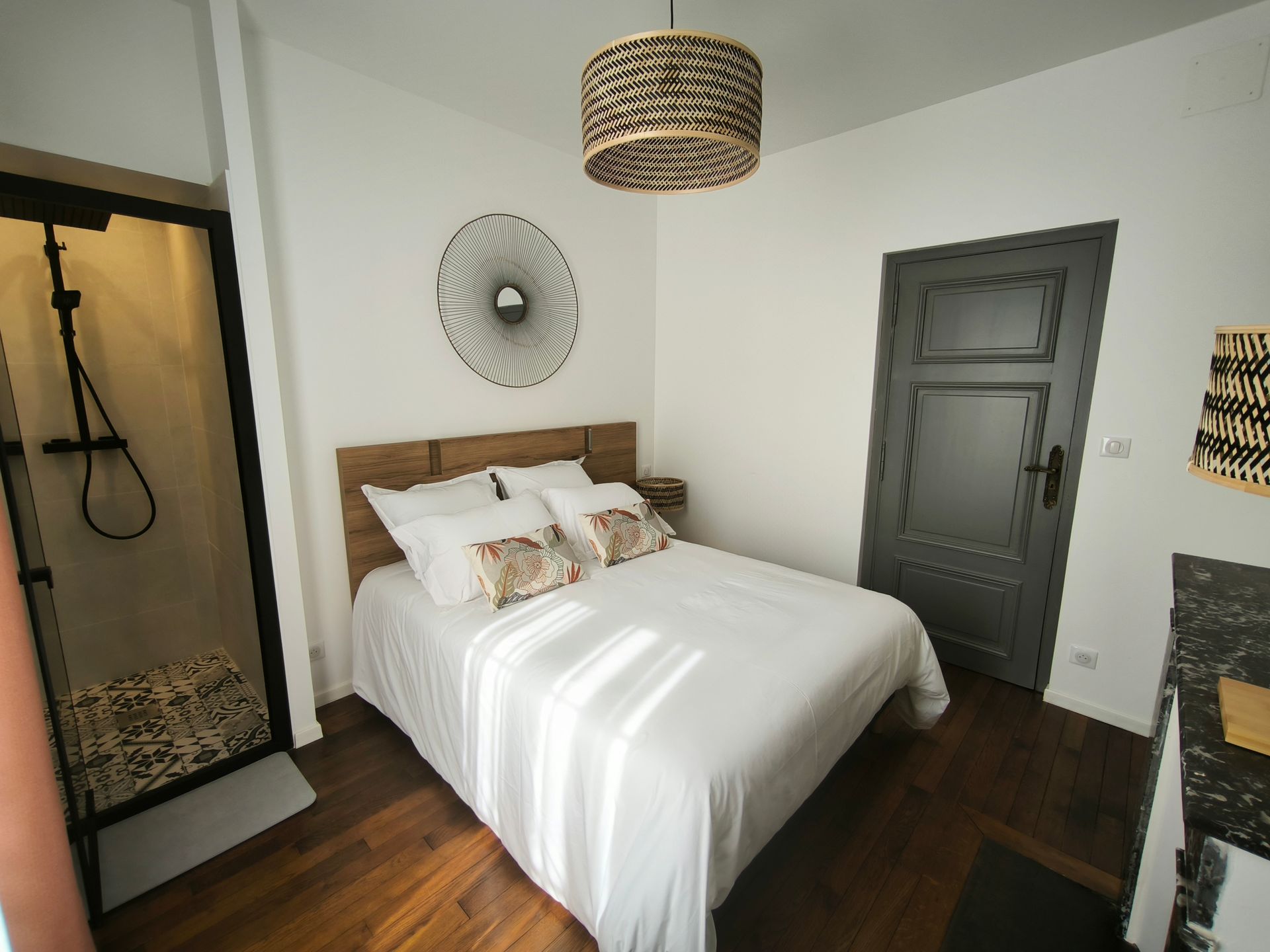Chambre confortable avec literie blanche, éléments en bois, porte de douche noire et portes gris foncé sur parquet.