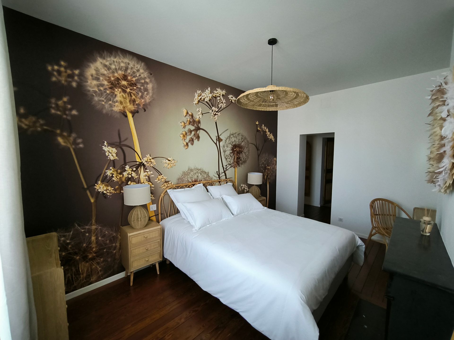 Chambre élégante avec lit blanc, fresque murale florale, éléments en osier et parquet foncé