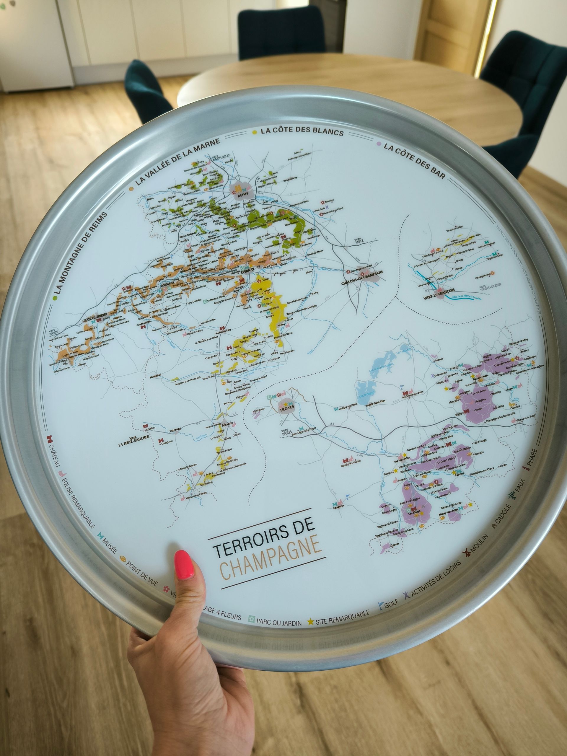 Une main tenant un plateau rond orné d'une carte du monde au-dessus d'une table dans une pièce lumineuse