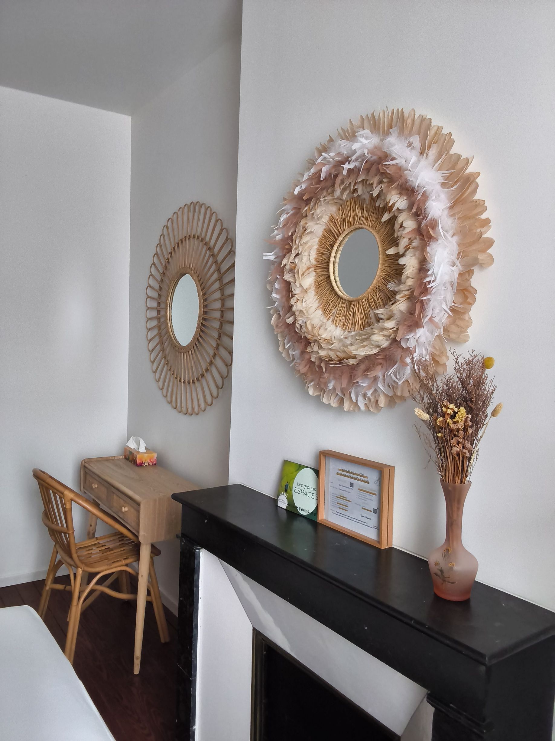 Entrée accueillante avec une console noire, un miroir rond en osier, un petit bureau, une chaise et un arrangement de fleurs séchées.