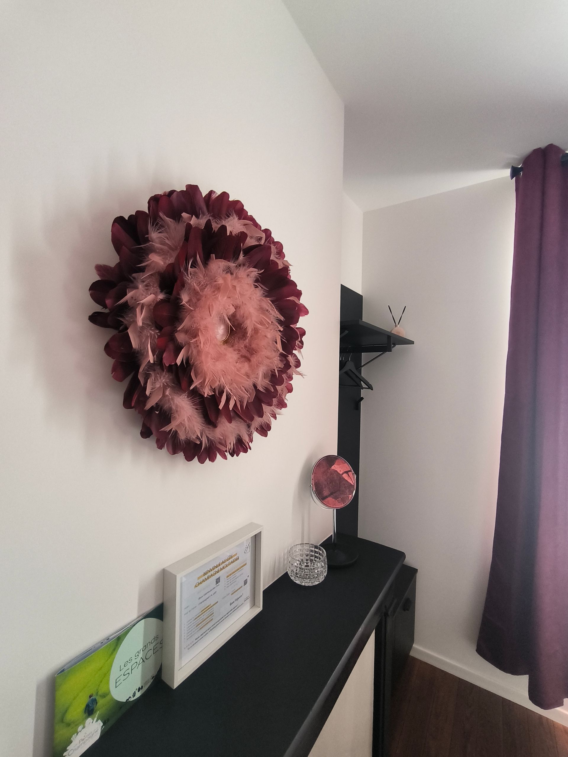 Un couloir étroit avec une console noire, des tableaux encadrés, une décoration murale florale rose et des rideaux violets.
