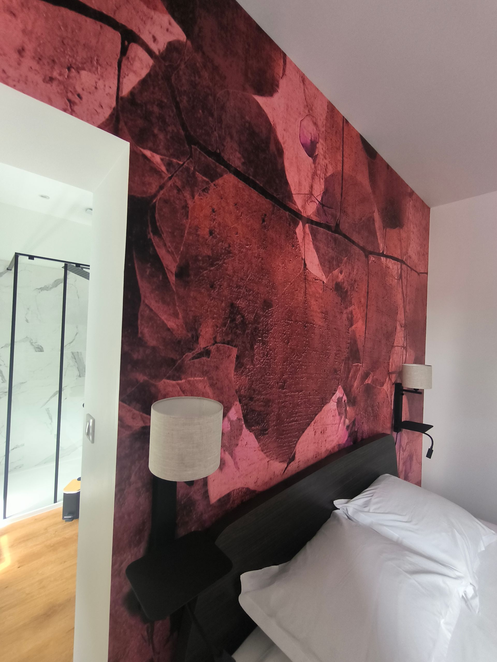 Mur de chambre orné d'une grande fresque abstraite rose derrière un lit aux oreillers blancs.