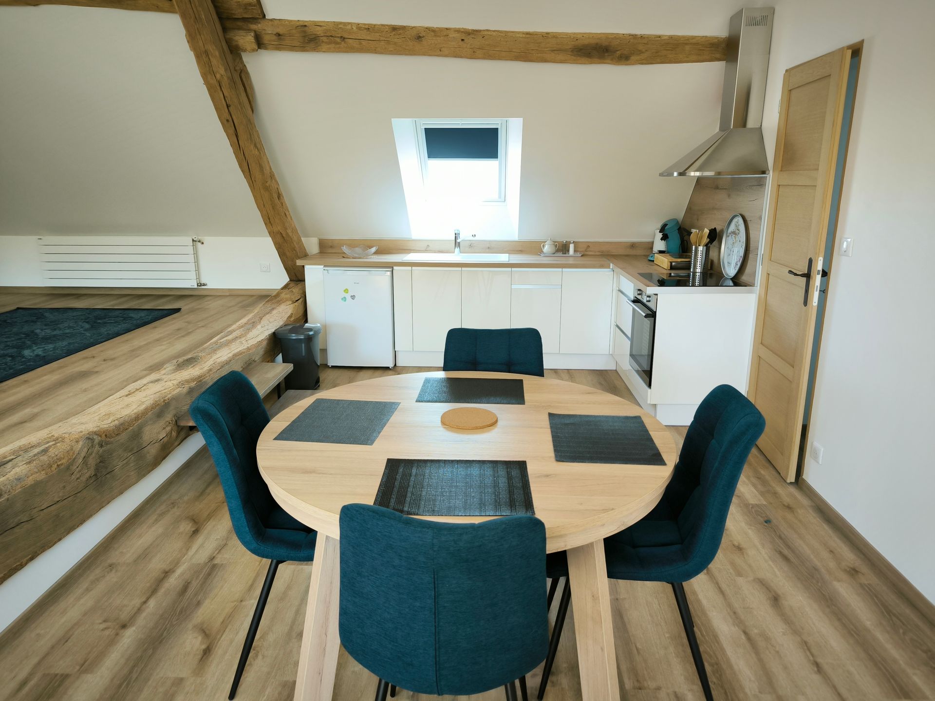 Petit coin repas avec une table en bois, des chaises turquoise et une chambre en mezzanine dans une chambre mansardée lumineuse