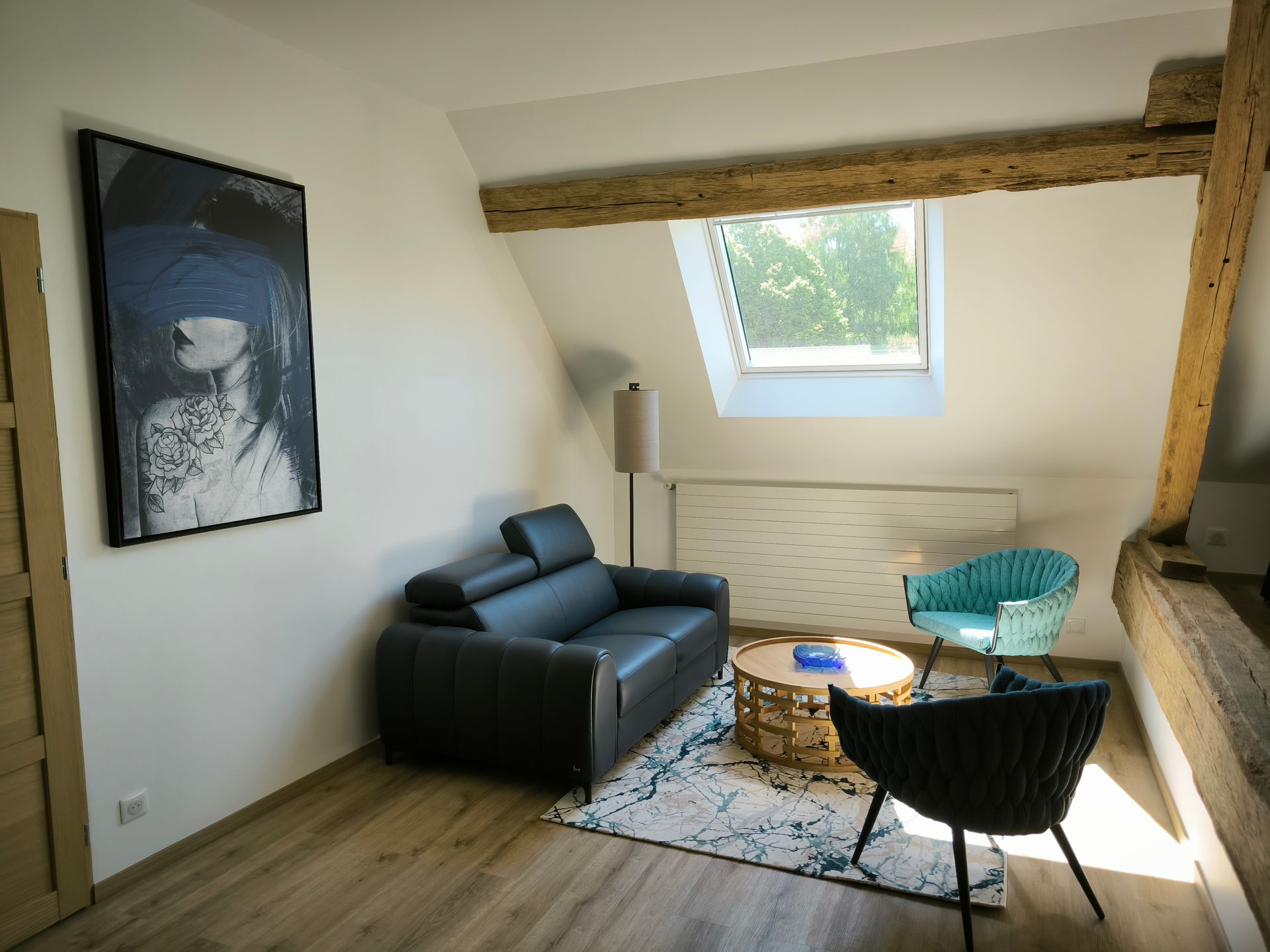 Salon loft confortable avec canapé noir, chaises en osier, petite table et puits de lumière