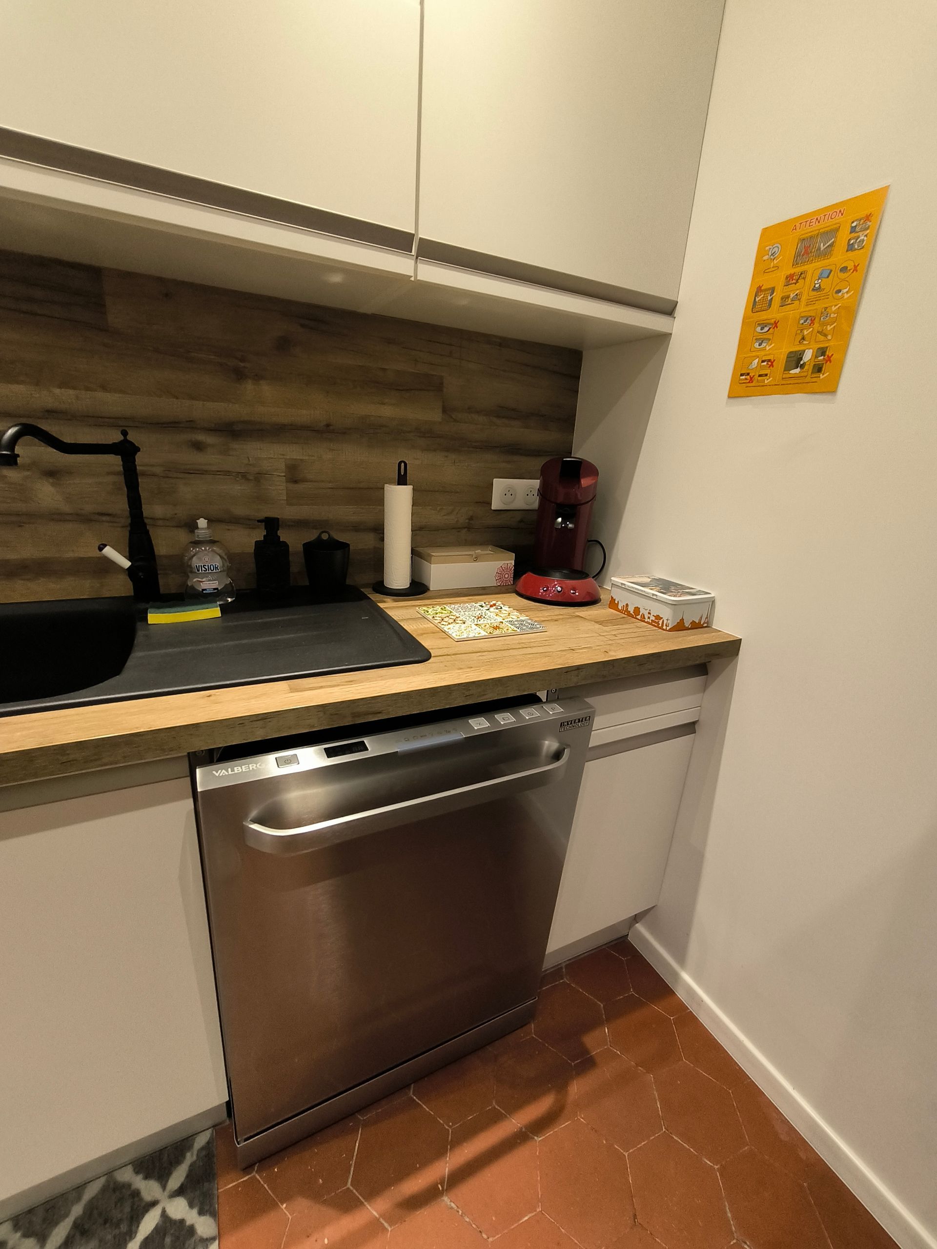 Coin cuisine compact avec lave-vaisselle en inox, évier, plan de travail en bois et décoration murale jaune.