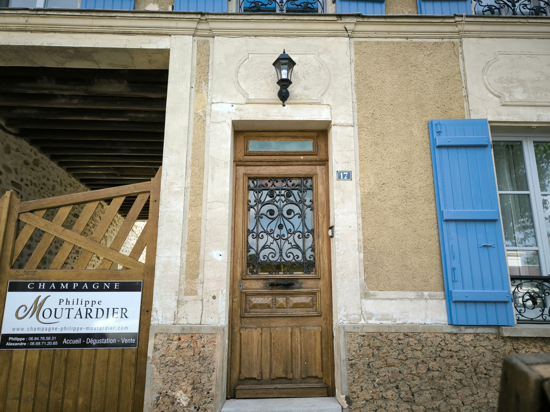 Porte d'entrée en bois avec vitrail, volet bleu et façade en pierre sur un bâtiment rustique