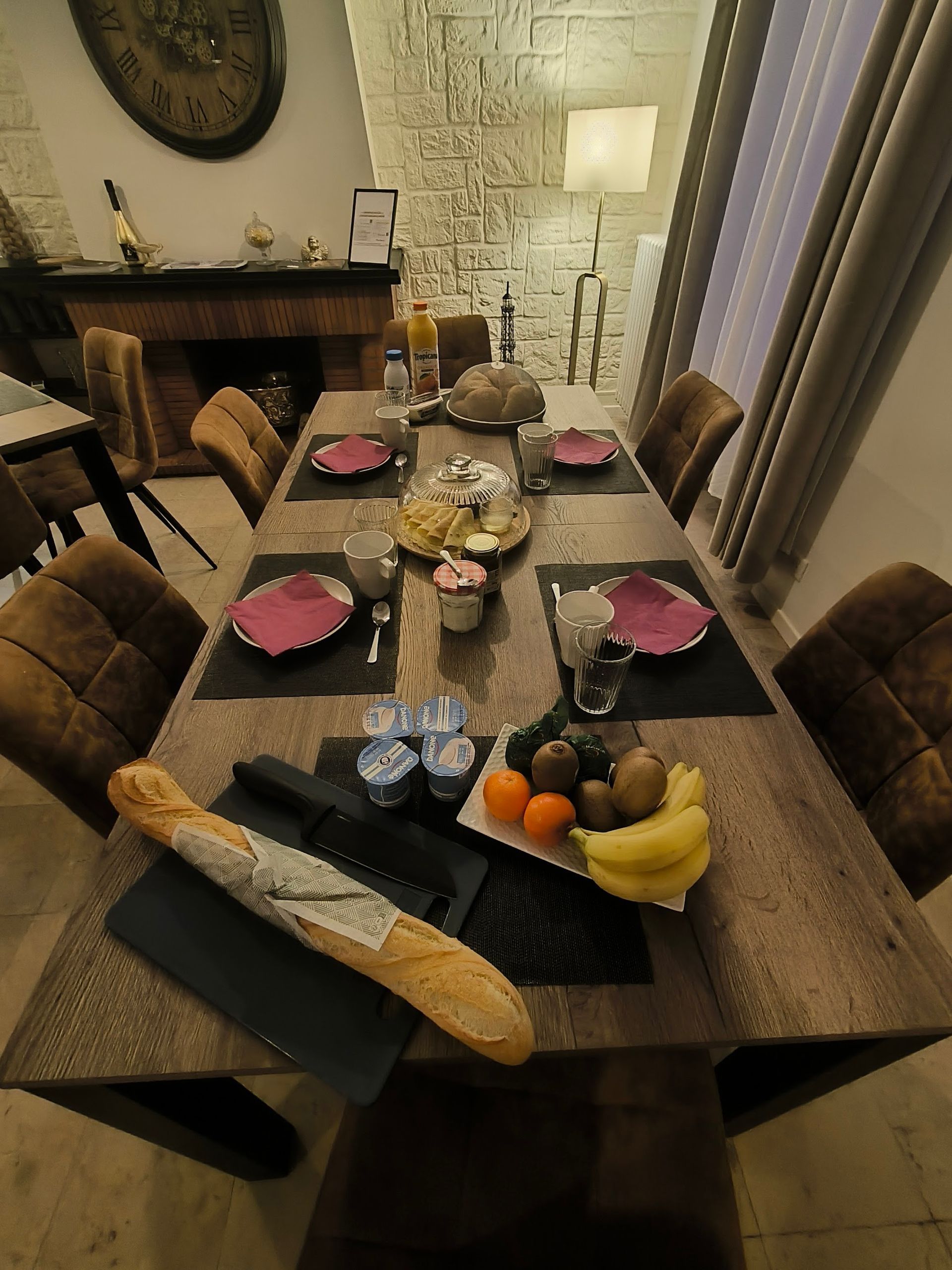 Dresser une table à manger avec une baguette, des fruits, des serviettes roses et des verres à vin dans une salle à manger confortable