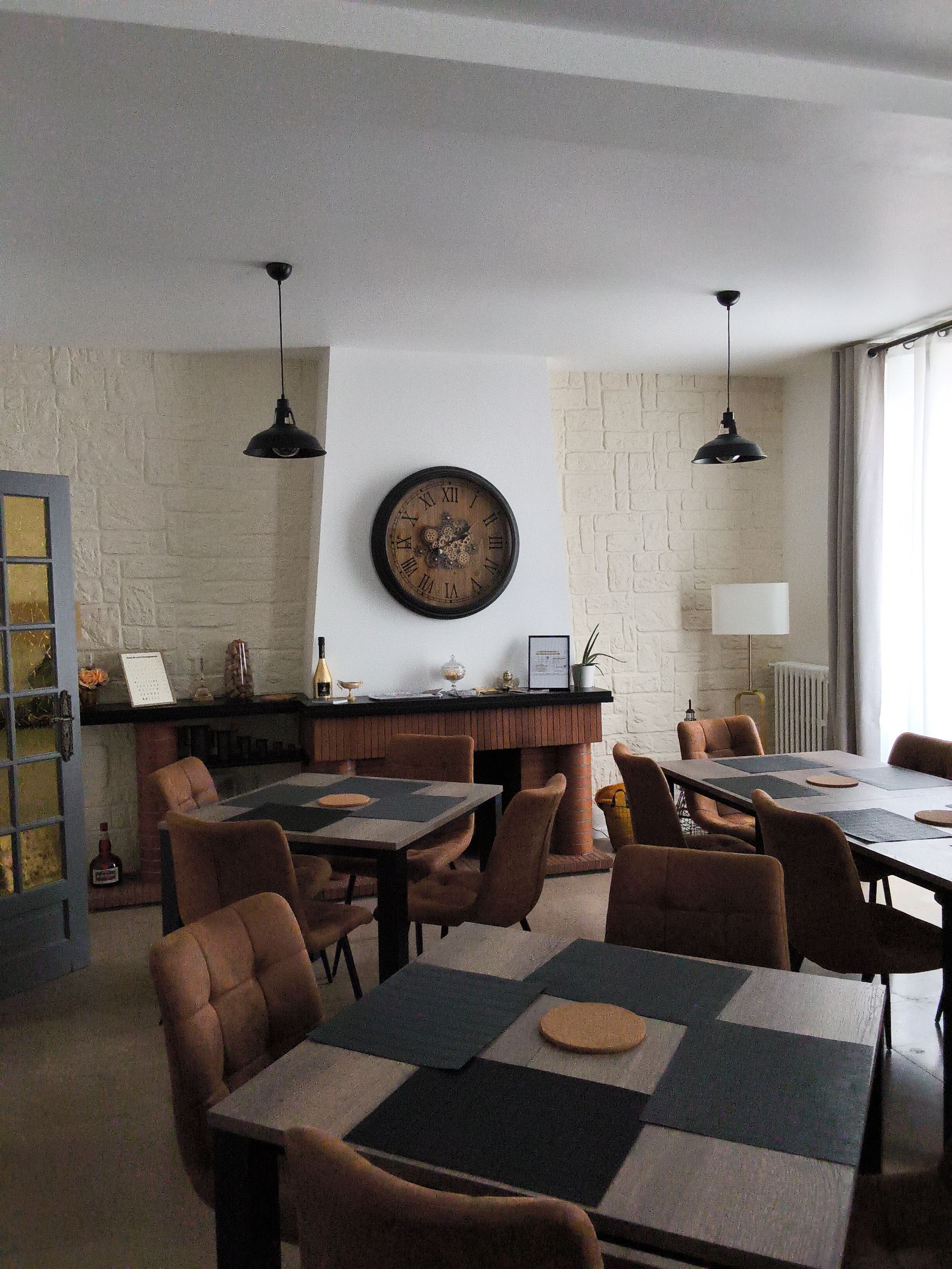 Salle à manger chaleureuse avec nappes à carreaux, chaises en bois, décorations murales et suspensions lumineuses près d'une fenêtre.