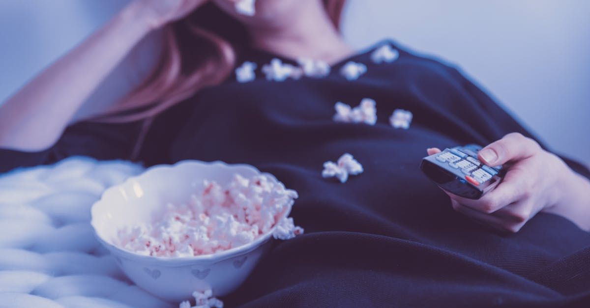 Eine Frau liegt mit einer Schüssel Popcorn und einer Fernbedienung auf einem Bett
