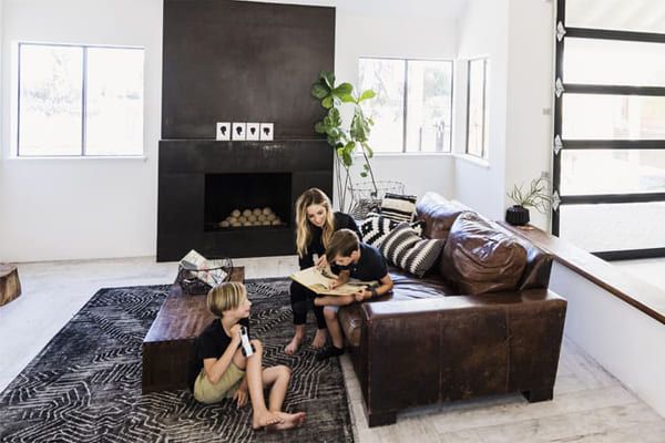 Famille dans le salon : femme et enfant regardant un livre ; un autre enfant sur le sol avec une tablette.