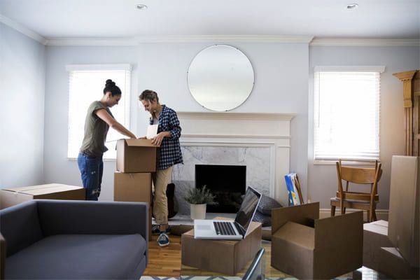 Couple déballant des cartons dans un salon avec une cheminée, un miroir et un ordinateur portable.