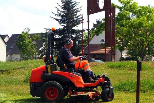 Un homme utilise une tondeuse à gazon orange vif pour couper l'herbe dans un parc.