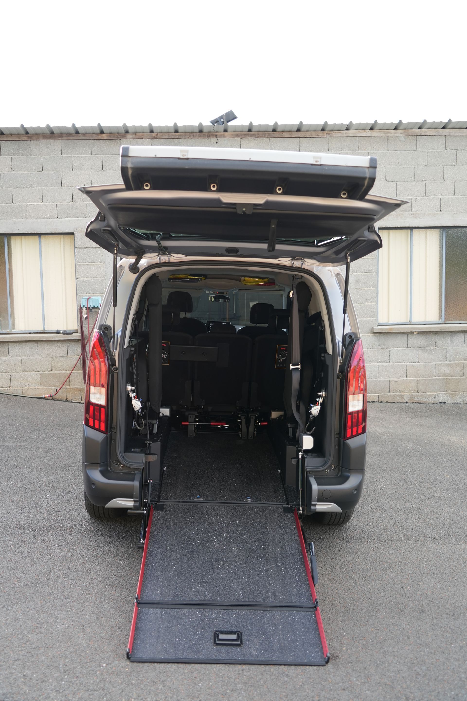 Fourgon avec les portes arrière ouvertes et la rampe dépliée jusqu’au sol pour permettre l’accès en fauteuil roulant