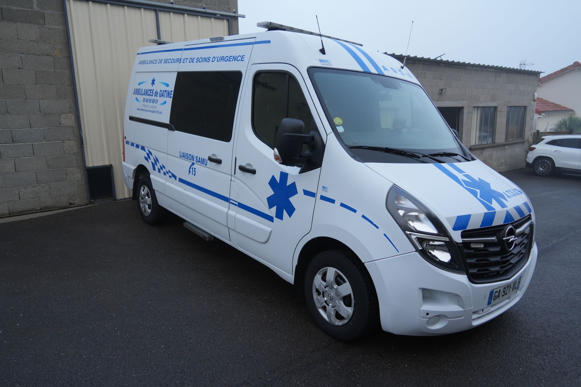 Une ambulance blanche stationnée devant un bâtiment, dans une rue mouillée