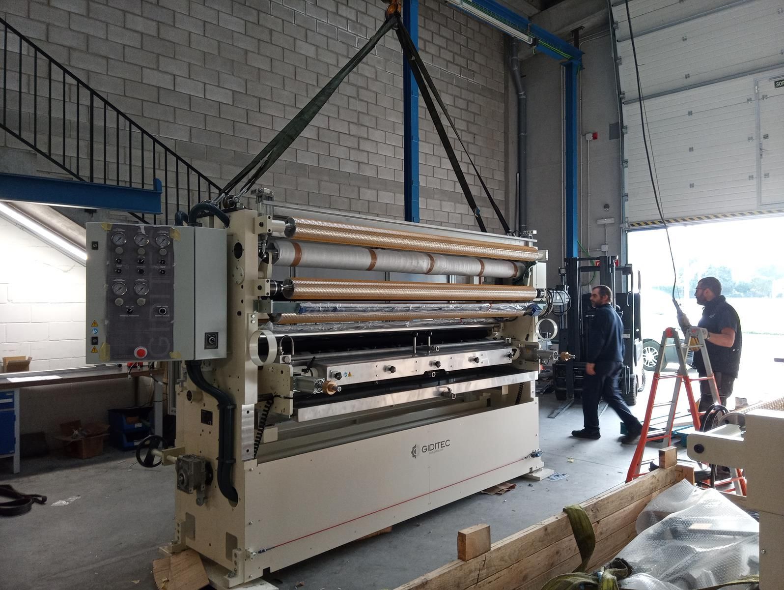 Una máquina grande está siendo levantada hacia un almacén mediante una grúa.