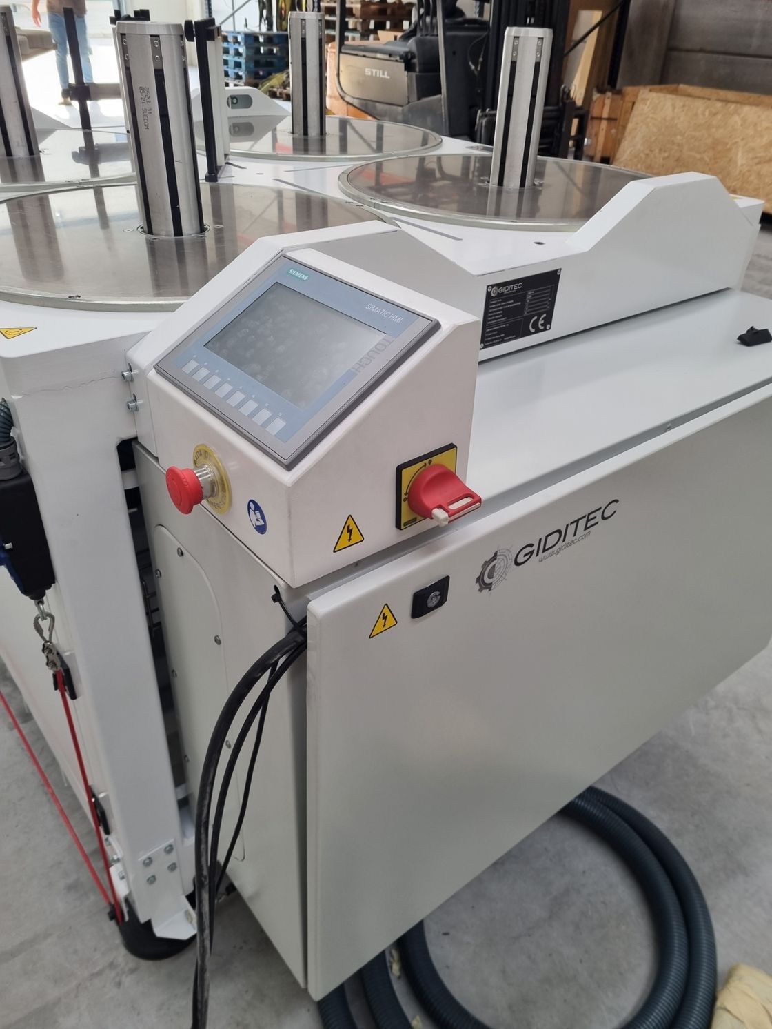 Una máquina blanca con un botón rojo en el costado está sobre un piso de concreto.