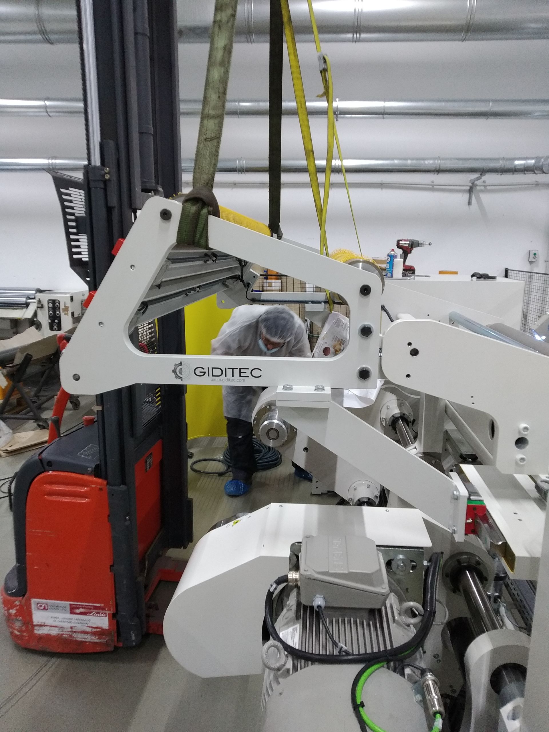 Un hombre está trabajando en una máquina en una fábrica al lado de una carretilla elevadora.