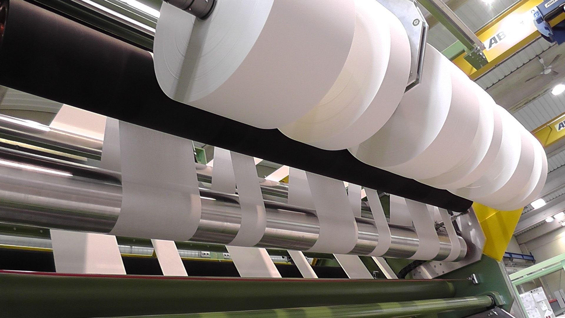 Se están cortando rollos de papel en una máquina en una fábrica.