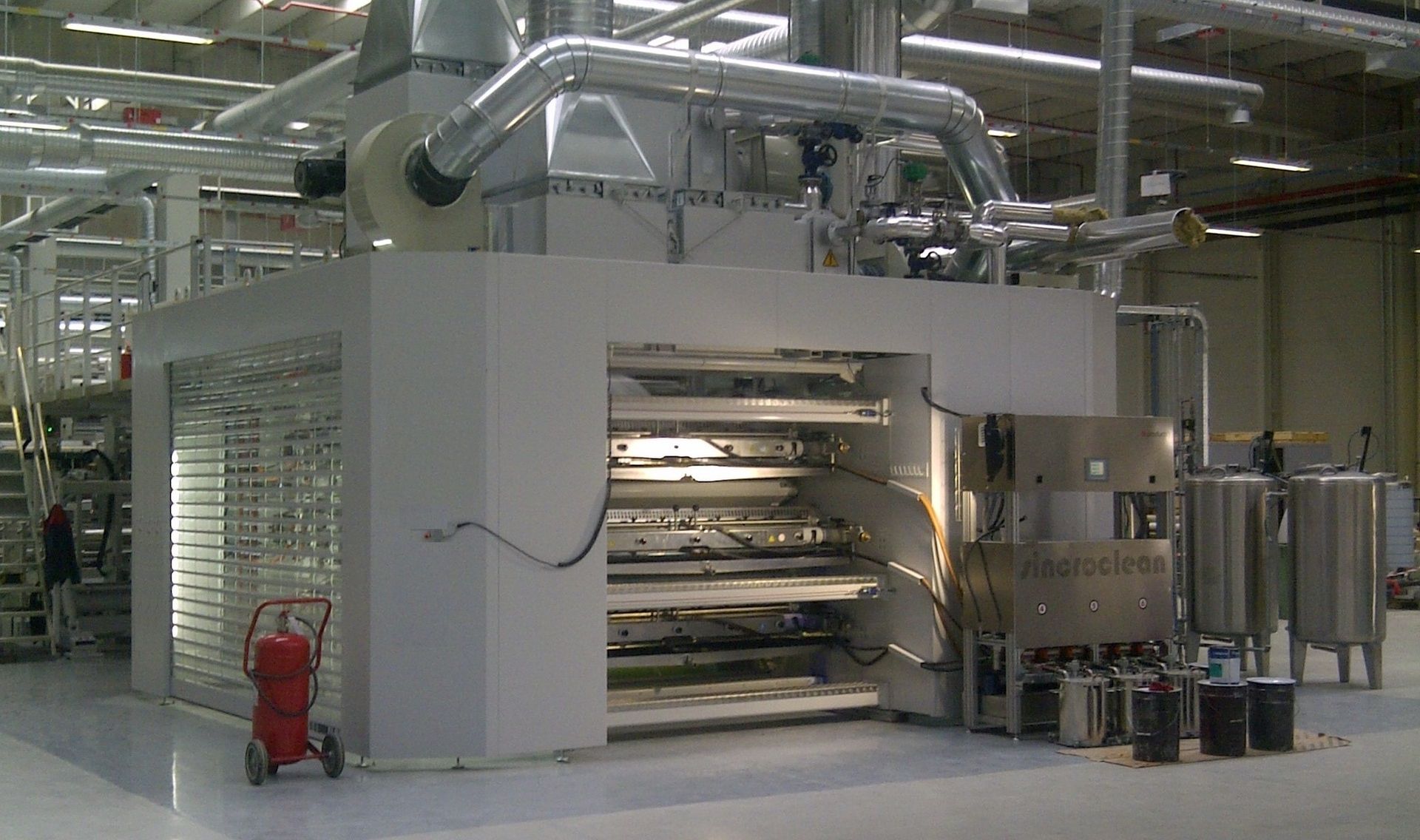 Una máquina grande en una fábrica con un extintor de incendios delante de ella.