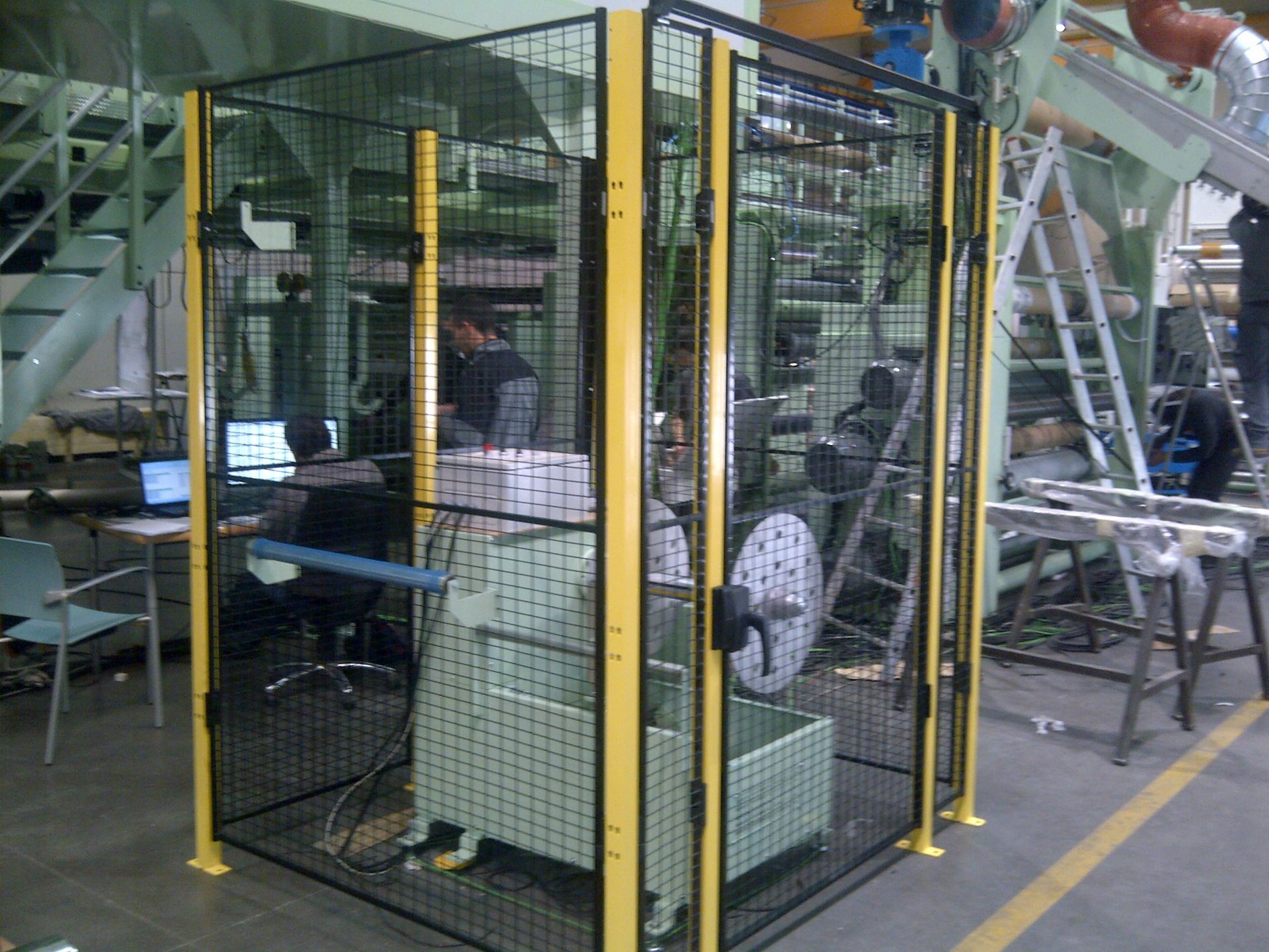 Un hombre está trabajando en una máquina dentro de una jaula en una fábrica.