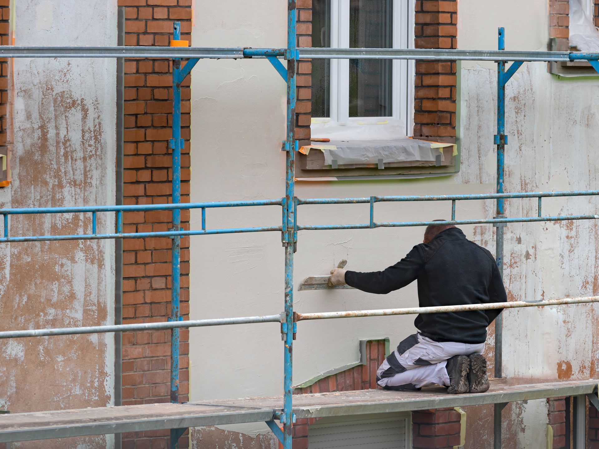 Un homme sur un échafaudage applique un revêtement sur le mur d'un bâtiment.