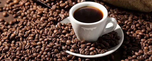 Una taza de café reposa sobre un platillo rodeada de granos de café.