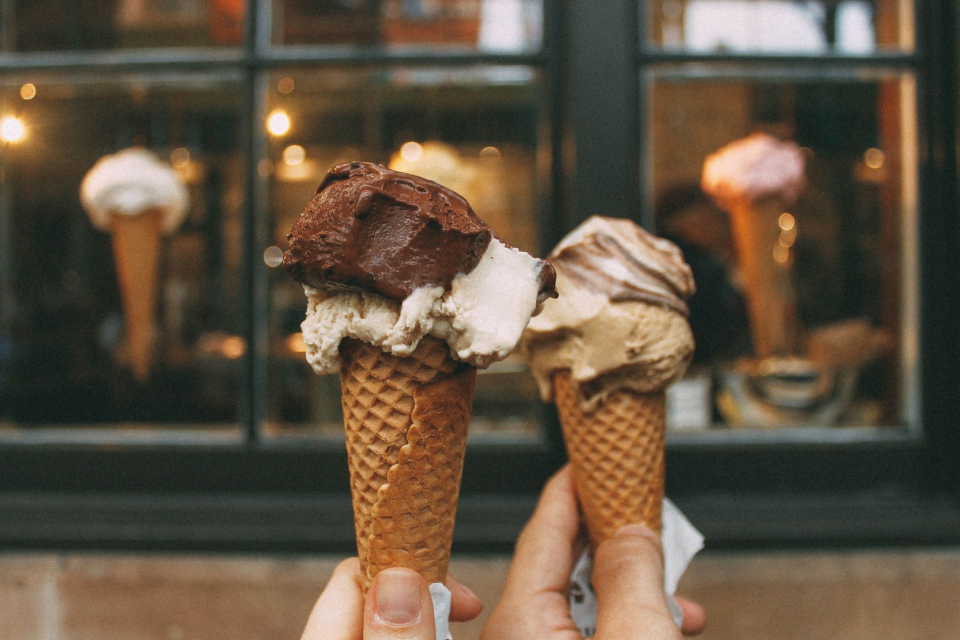 Una persona sostiene dos conos de helado frente a una ventana.