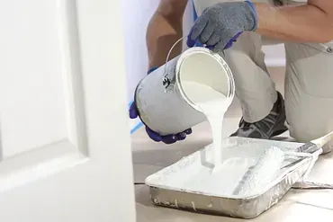 Henkilö kaataa maalia maaliastiaan