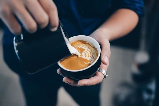 Una persona está vertiendo leche en una taza de café.