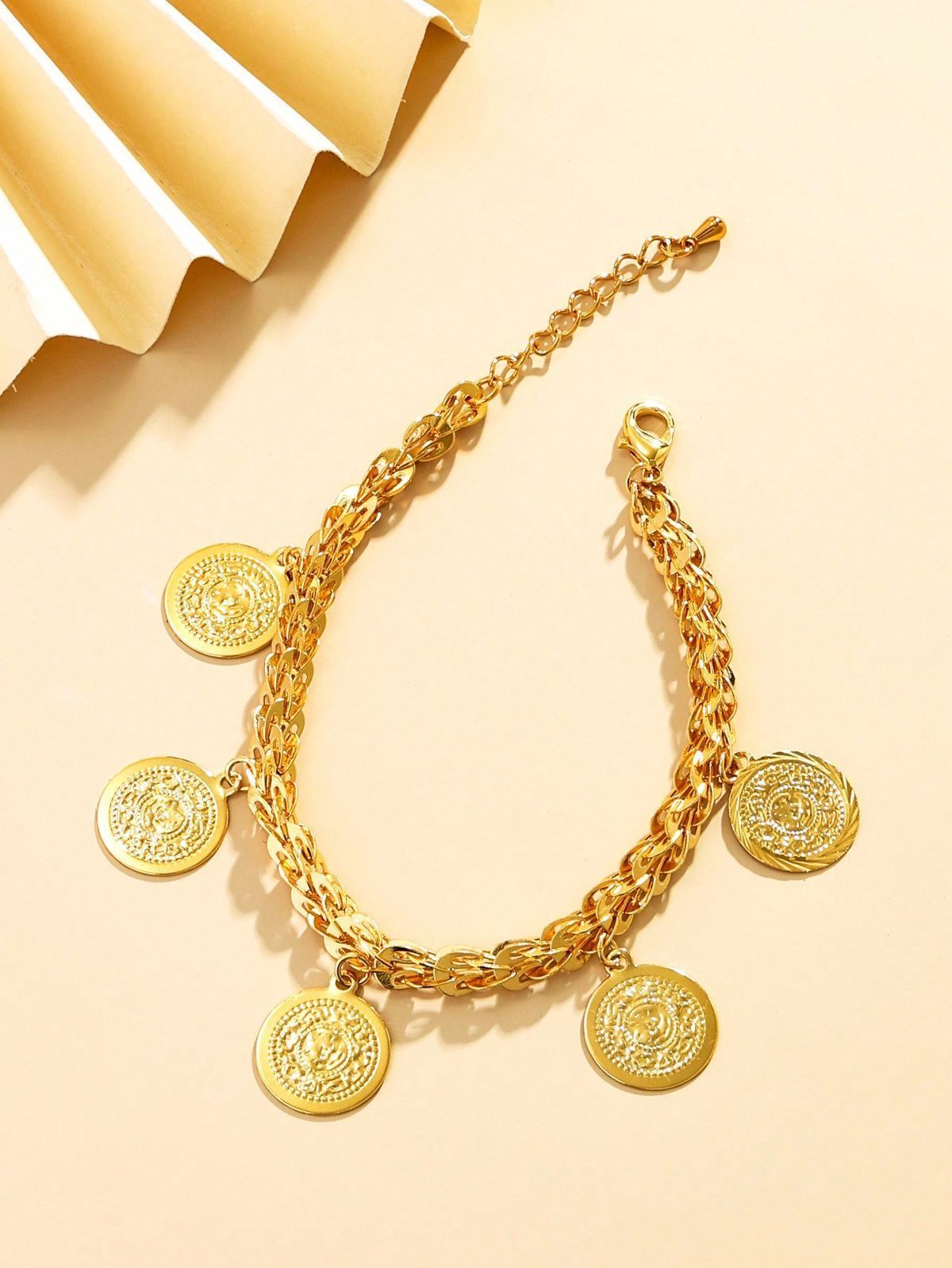 Una pulsera de oro con monedas está sobre una mesa al lado de un ventilador.