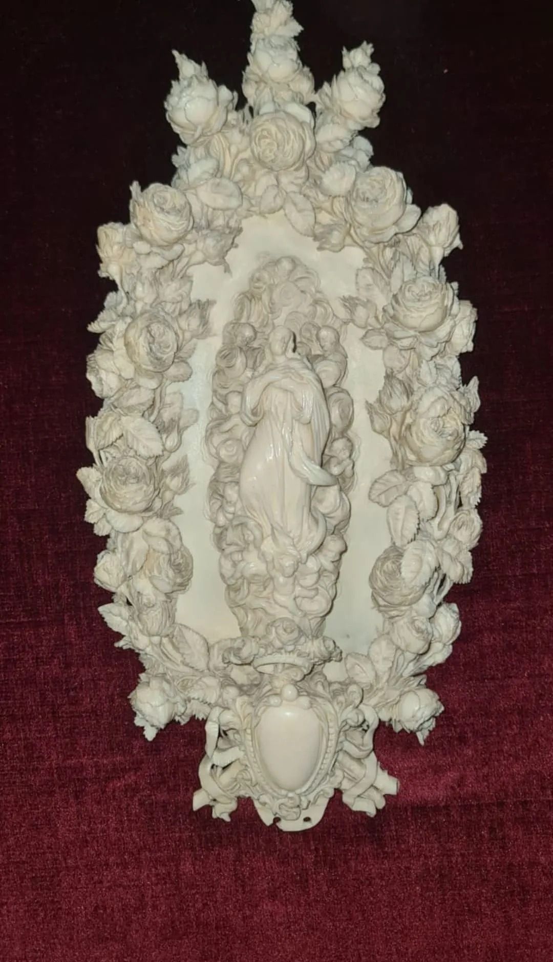 Una estatua de una mujer rodeada de rosas sobre una superficie roja.