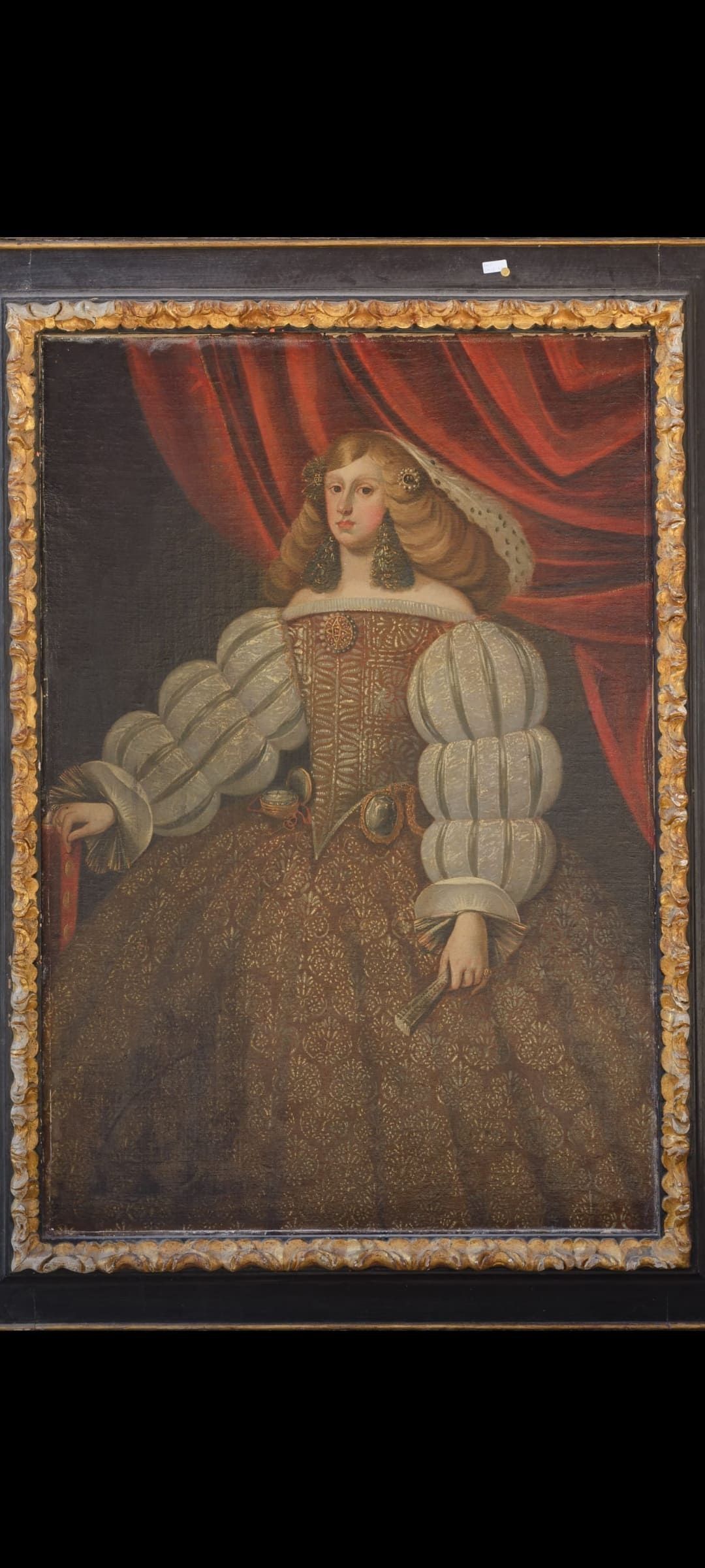 Un cuadro enmarcado de una mujer con un vestido sentada frente a una cortina roja.