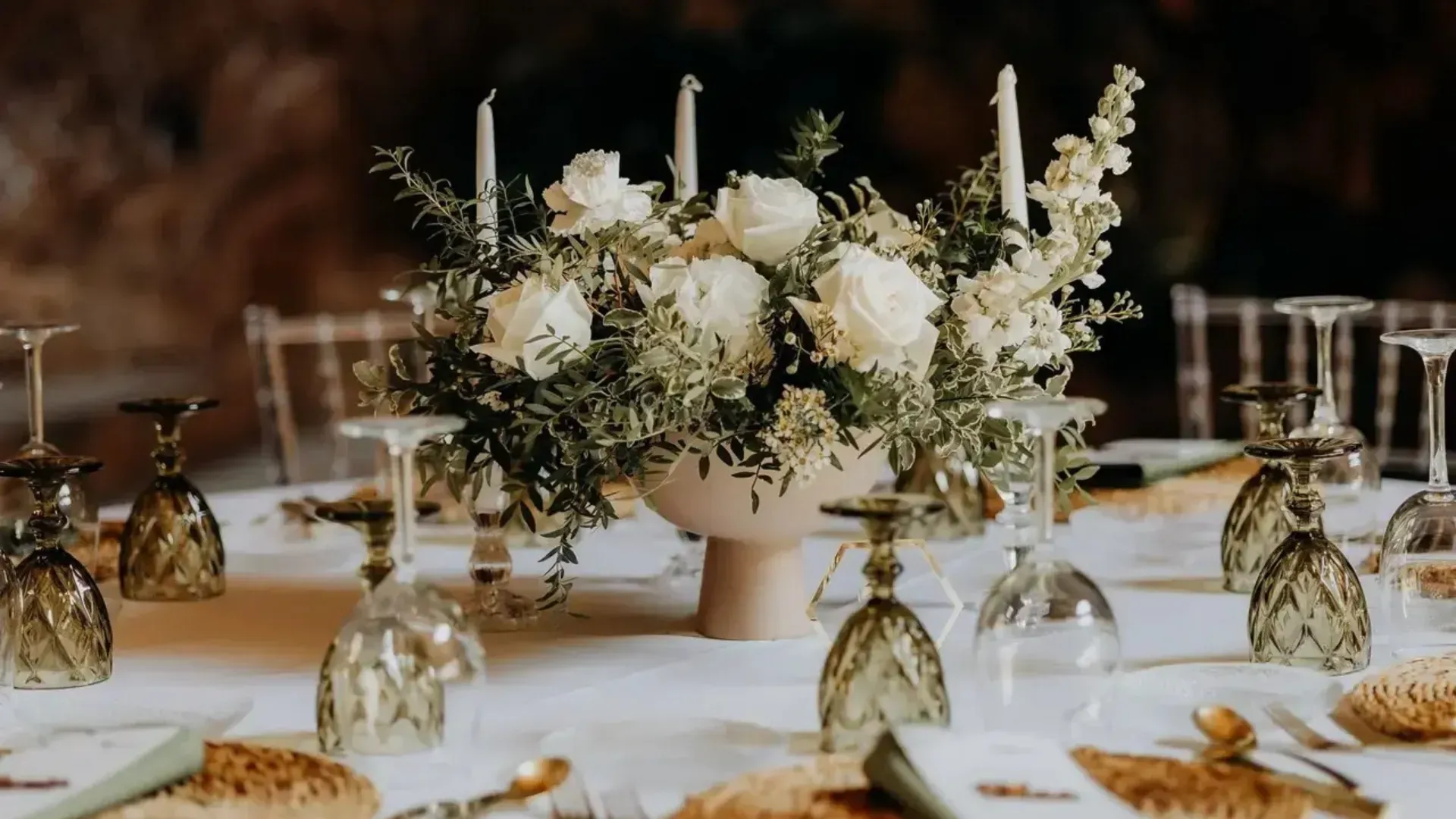 Elegante mesa con centro de mesa floral blanco y cristalería verde vintage.
