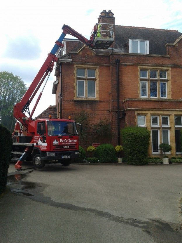 Red crane truck lifting a worker to the roof of a brick house