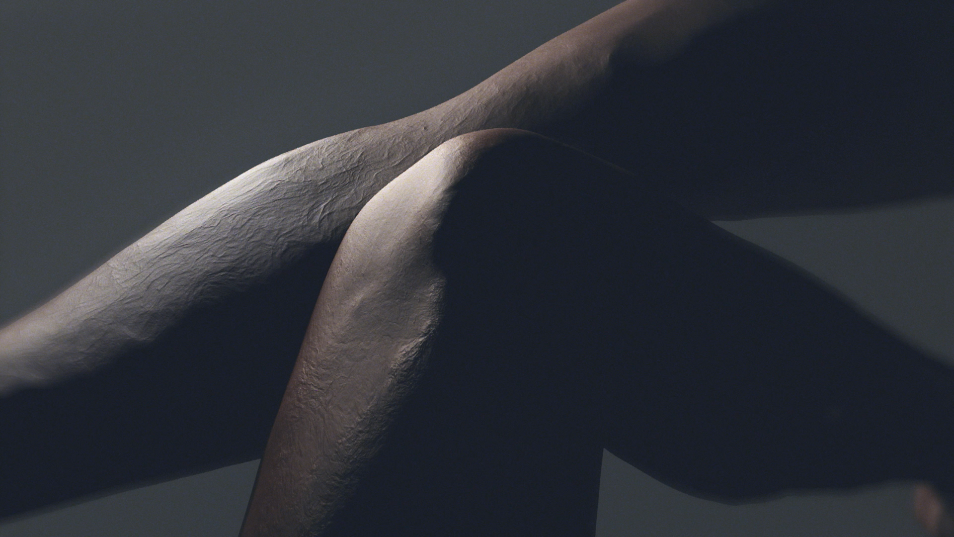 Piernas cruzadas, piel oscura, iluminada por una luz tenue. Rodillas enfocadas, juego de sombras.