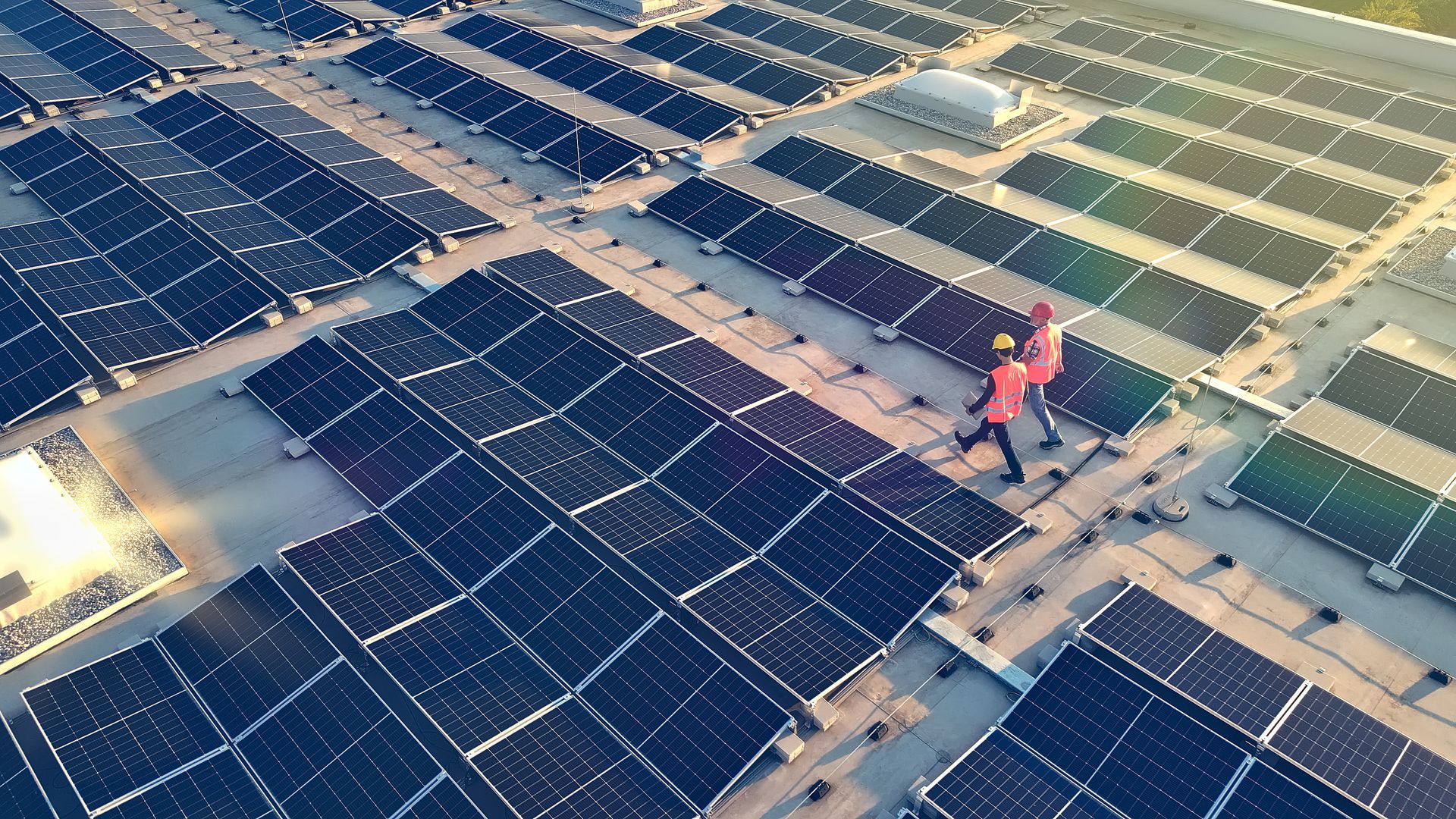 Des ouvriers du bâtiment sur le toit d'un immeuble utilisent un ascenseur. Une grue jaune et un bâtiment aux fenêtres vitrées sont visibles.