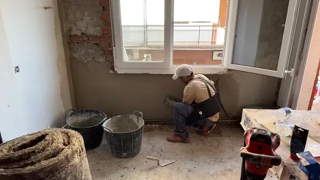Un hombre está arrodillado en el suelo en una habitación al lado de una ventana.