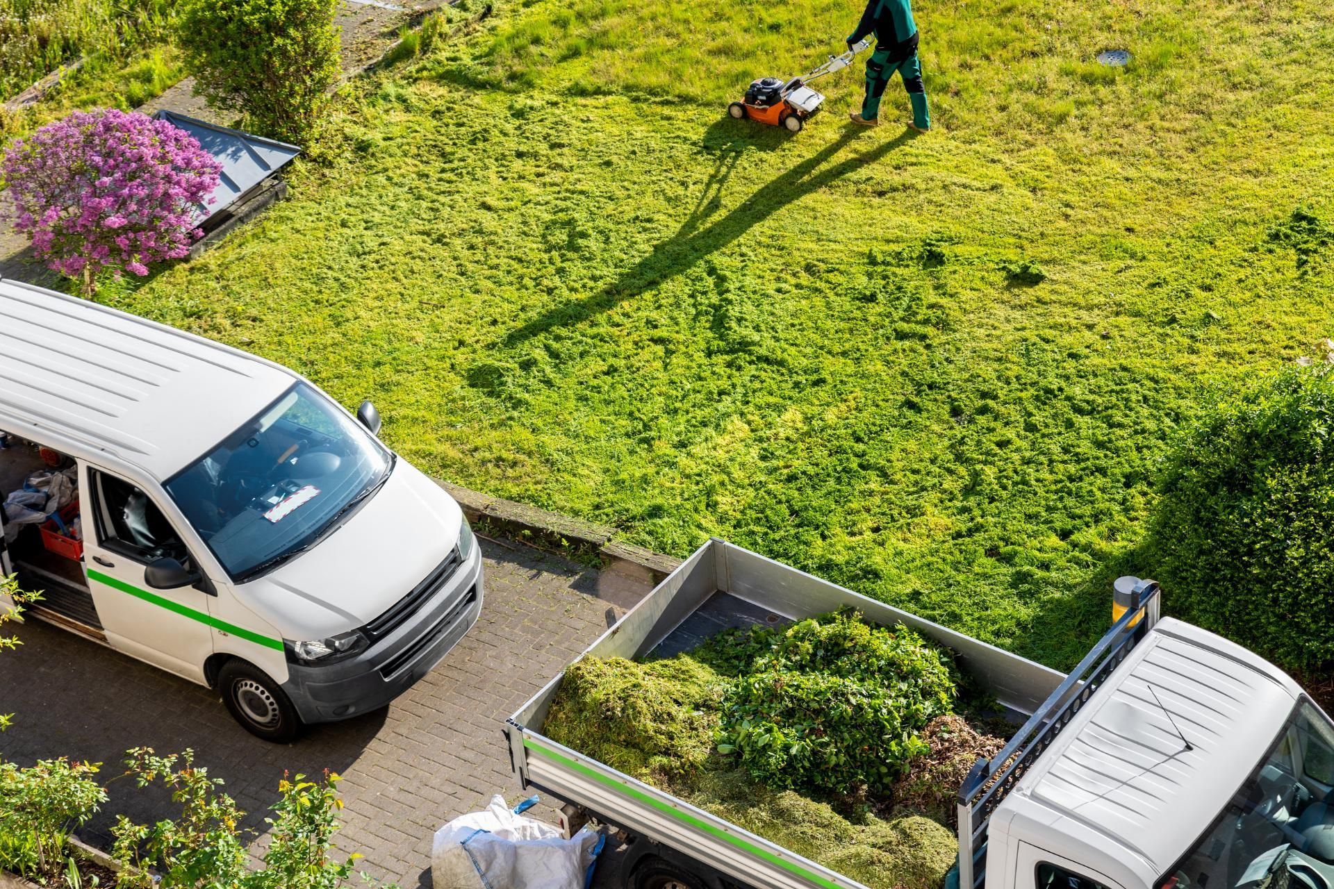Ein Mann mäht das Gras neben einem mit Gras beladenen Lastwagen.
