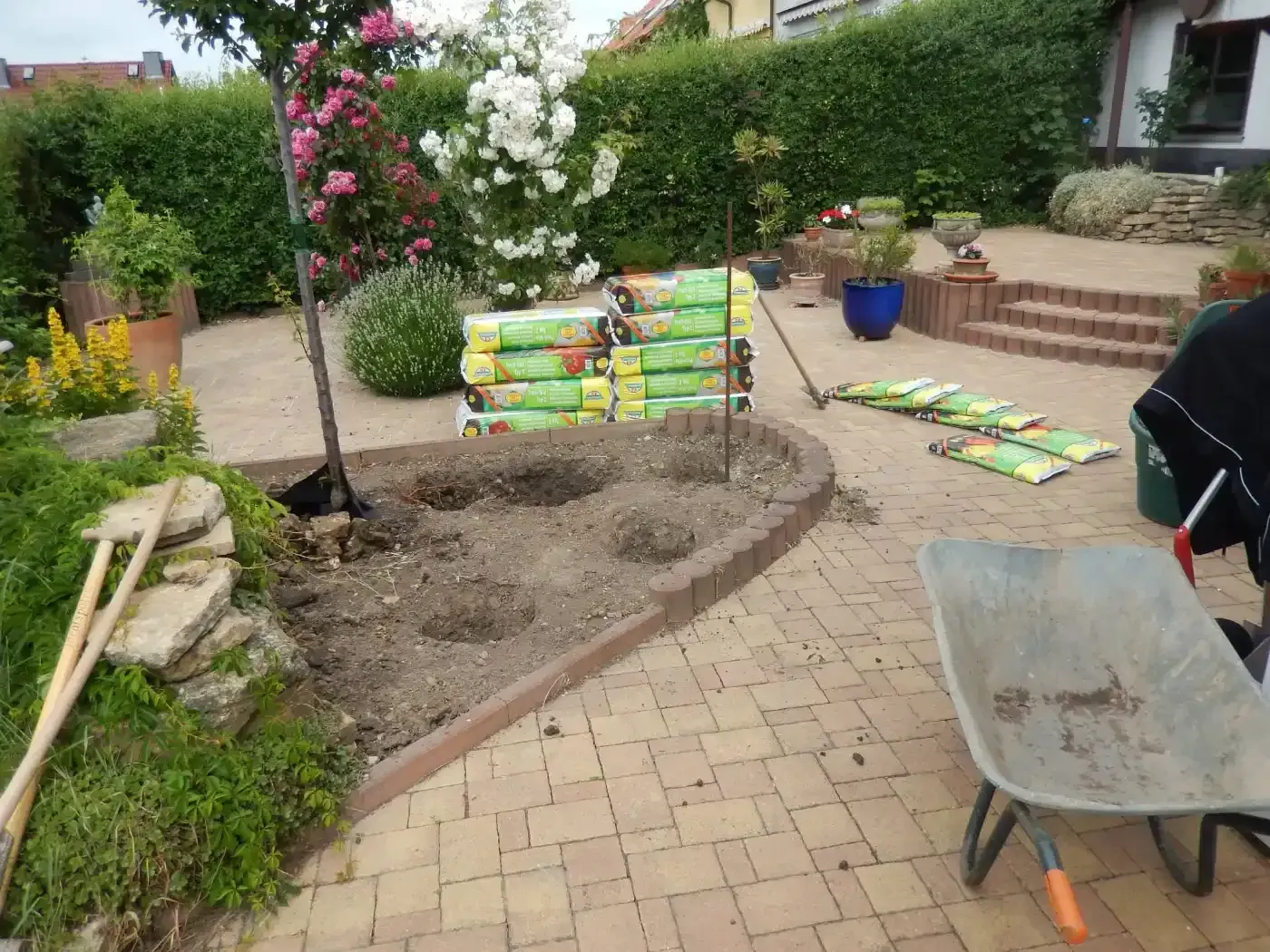 Eine Person arbeitet mit einer Schubkarre und einer Schaufel in einem Garten.