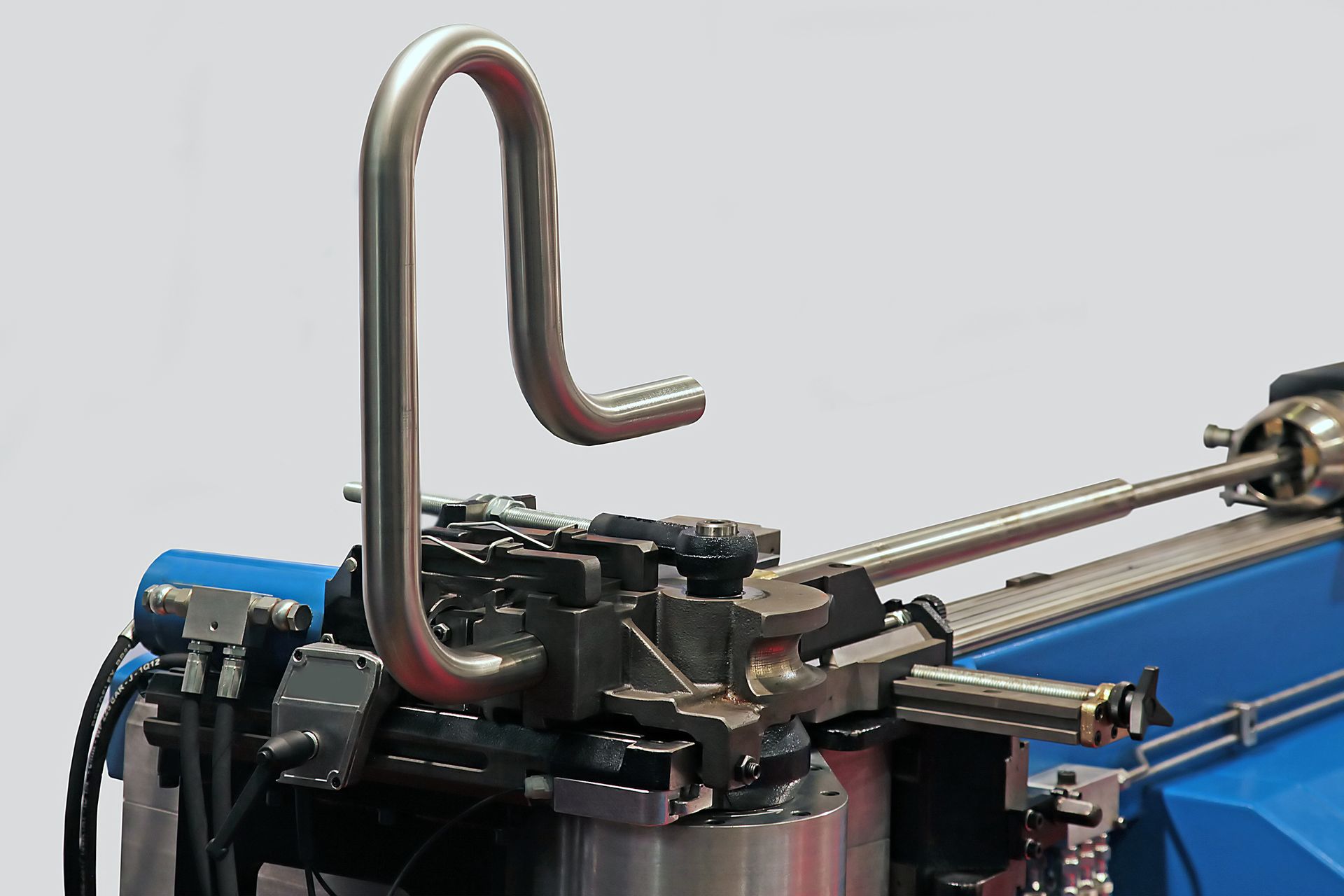 Nahaufnahme einer blauen Industriemaschine mit einem gebogenen Metallrohr und daran befestigten Schläuchen.
