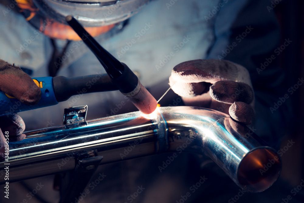 Eine Person schweisst mit einem Schweissbrenner und Schutzhandschuhen ein glänzendes Metallrohr.