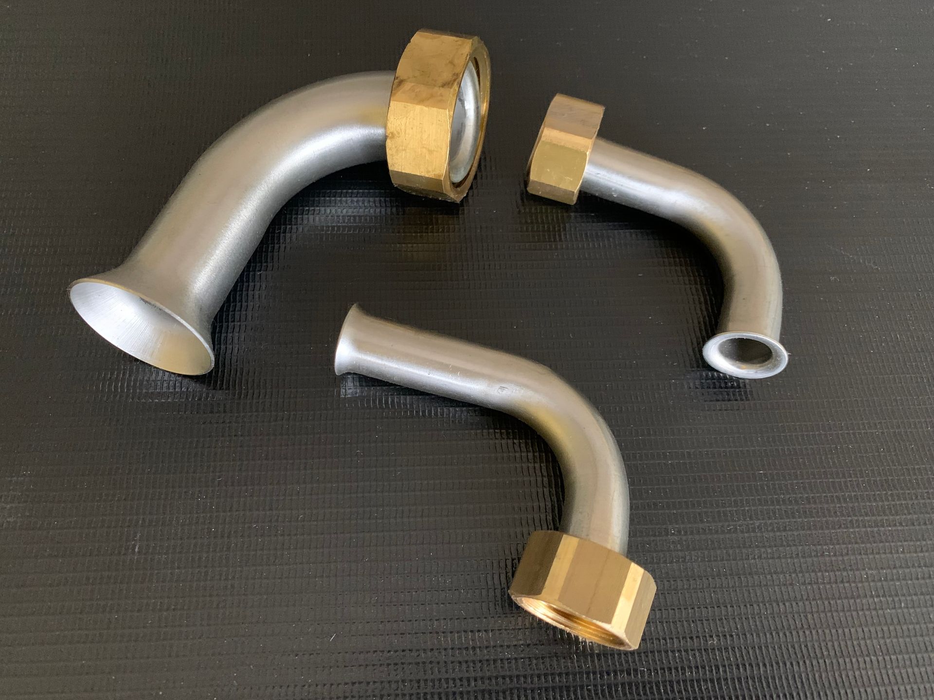 Drei gebogene Metallstäbe mit silberner und goldener Oberfläche auf dunklem Untergrund